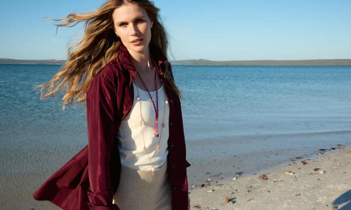 Modelo con camisa burdeos y joyas de las colecciones India y Mikado de Tamara Comolli paseando junto al mar